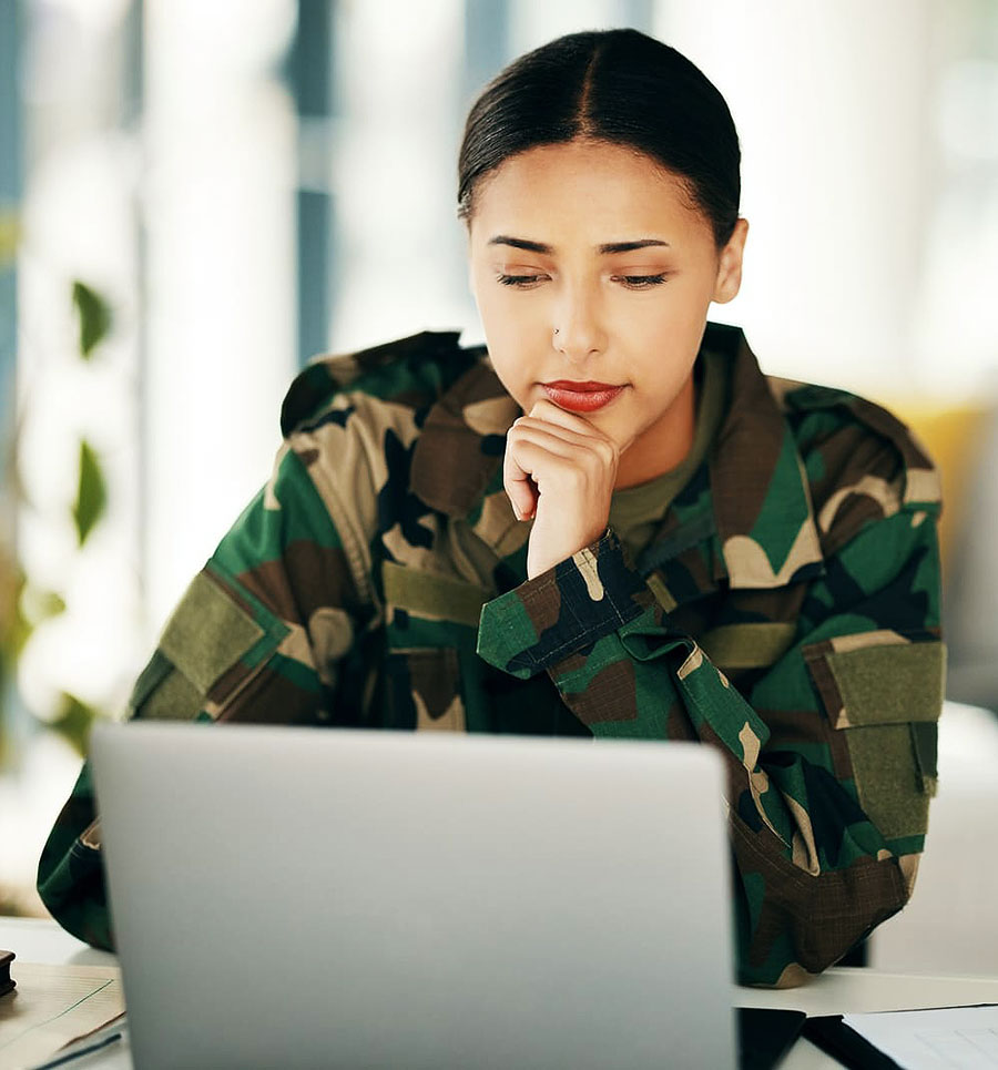 A service member in uniform working through paperwork on a laptop.